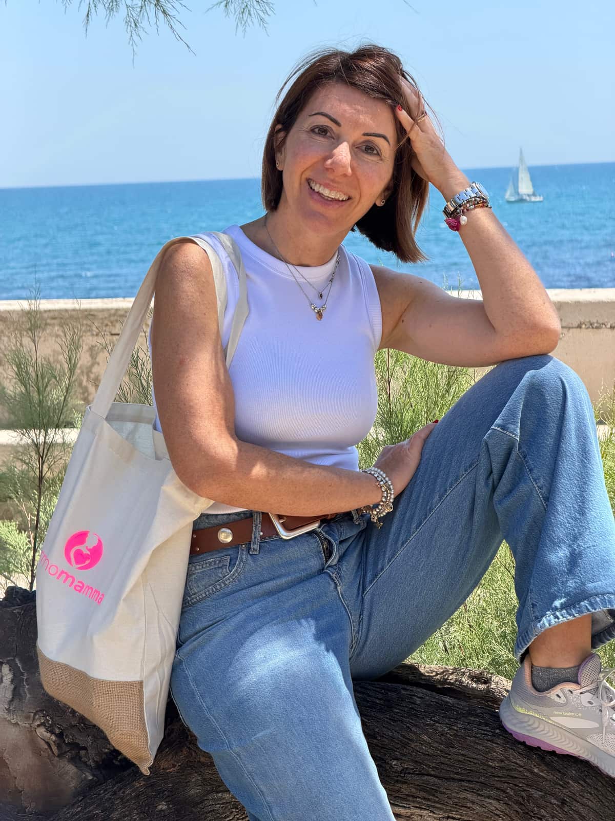 Fulvia, fondatrice di Dermomamma, seduta in riva al mare con la shopper Dermomamma