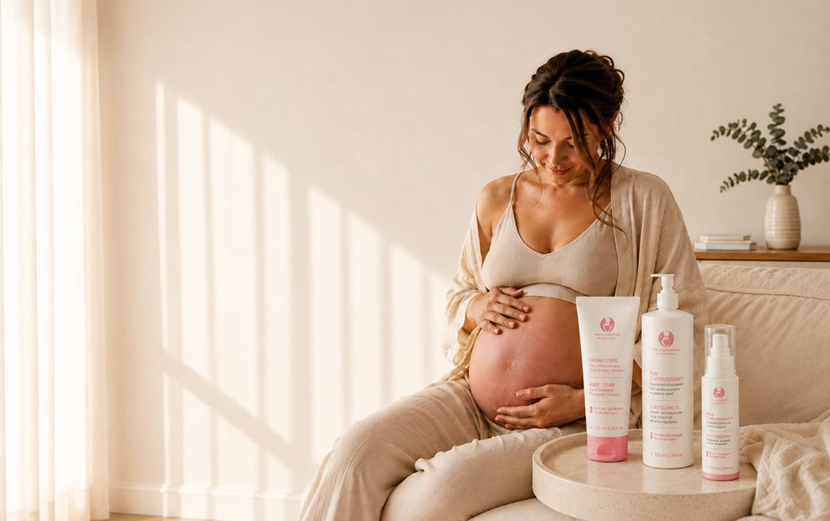 Futura mamma sul divano accarezza il pancione accanto a crema corpo, olio elasticizzante e siero Dermomamma